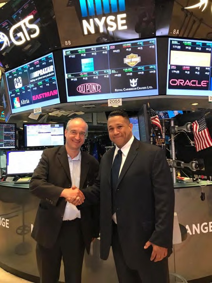 Asa Saint Clair shaking hands with Roland Schatz on the trading floor of the New York Stock Exchange.
