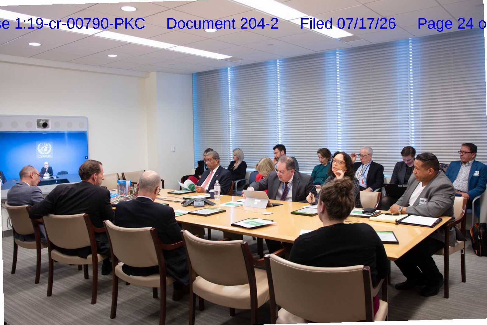 A working meeting around a conference table inside UN headquarters, a UN video screen at left; Asa Saint Clair sits at right in a gray jacket.